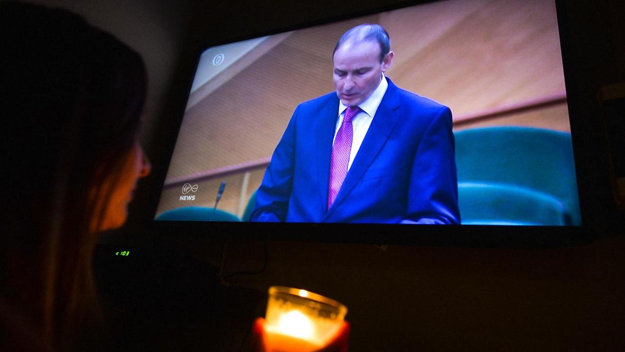 Ein Frau, die eine Kerze hält, schaut sich die Rede von Micheal Martin im Fernsehen an. Ein Frau, die eine Kerze hält, schaut sich die Rede von Micheal Martin im Fernsehen an.