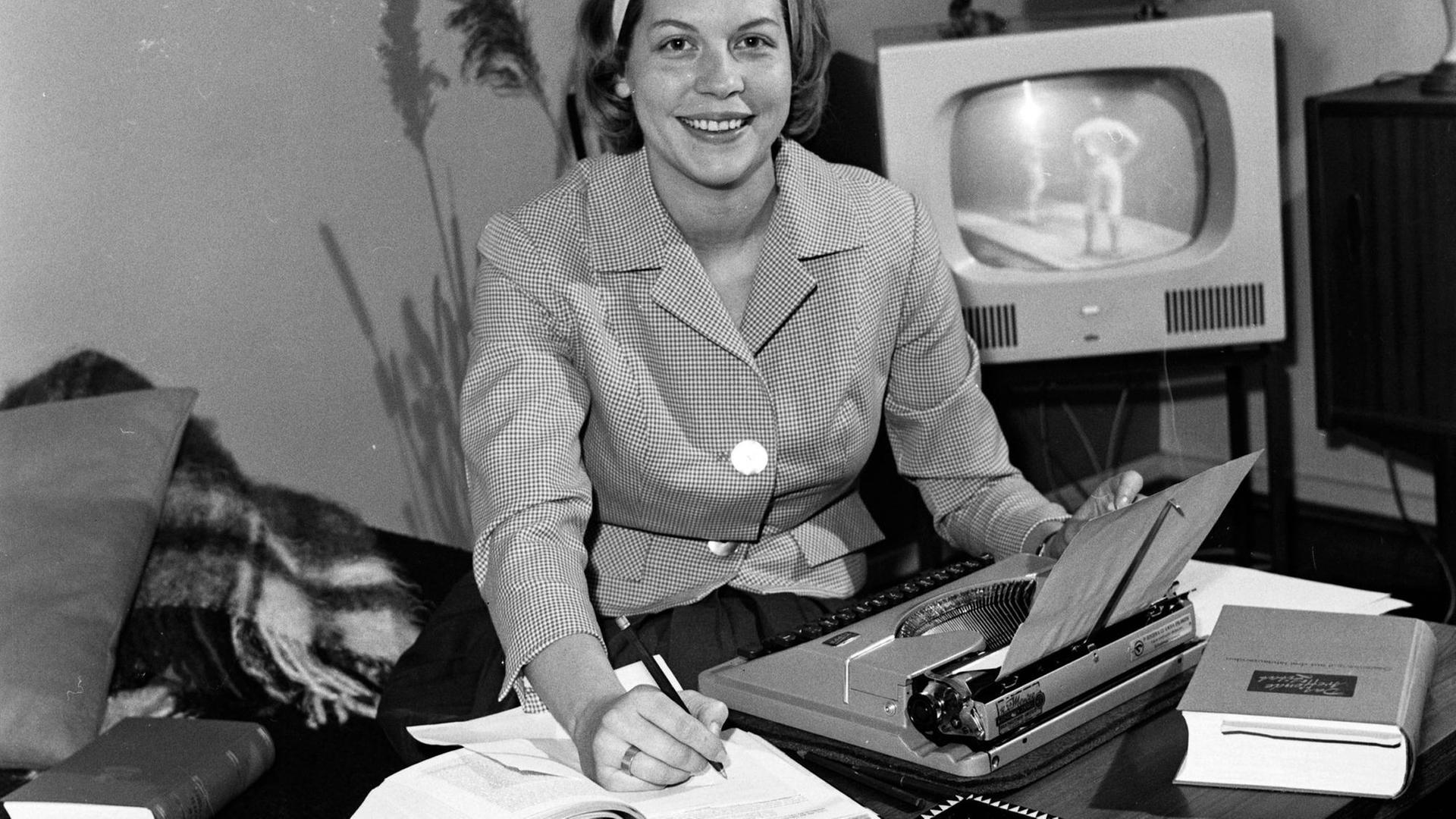 Homeoffice historisch: Eine junge Frau sitzt am Wohnzimmertisch mit Schreibmaschine und aufgeschlagenen Büchern, Deutschland 1960er Jahre. Homeoffice historisch: Eine junge Frau sitzt am Wohnzimmertisch mit Schreibmaschine und aufgeschlagenen Büchern, Deutschland 1960er Jahre.