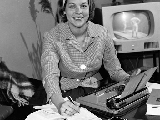 Homeoffice historisch: Eine junge Frau sitzt am Wohnzimmertisch mit Schreibmaschine und aufgeschlagenen Büchern, Deutschland 1960er Jahre.