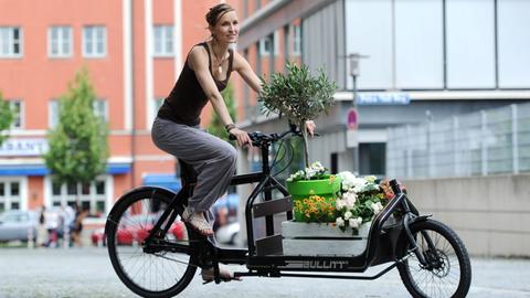 Eine Frau fährt mit einem Transportrad, das mit Blumen beladen ist.