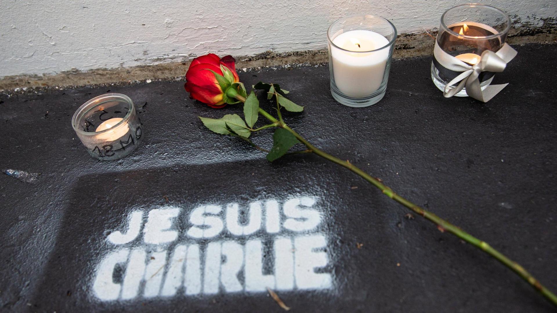 Eine Rose und Kerzen stehen auf der Straße, darunter der Schriftzug "Je suis Charlie" Eine Rose und Kerzen stehen auf der Straße, darunter der Schriftzug "Je suis Charlie"