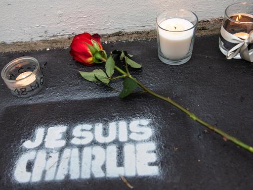 Eine Rose und Kerzen stehen auf der Straße, darunter der Schriftzug "Je suis Charlie"