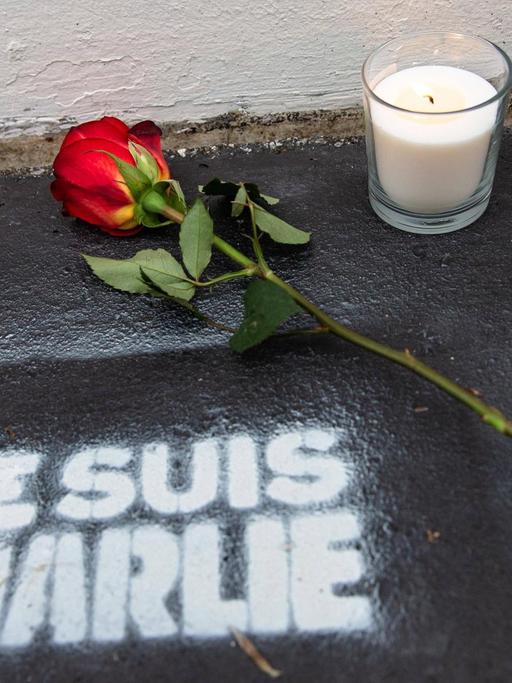 Eine Rose und Kerzen stehen auf der Straße, darunter der Schriftzug "Je suis Charlie"