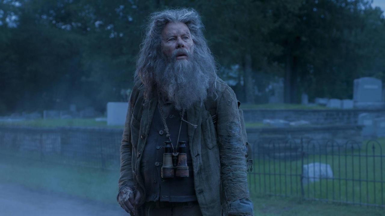 Tom Waits steht in der Horrorkomödie "Die Toten sterben nicht" aus dem Jahr 2019 von Jim Jarmusch mit langem Bart und zerzaustem langen Haar auf einer Straße im Dämmerlicht.