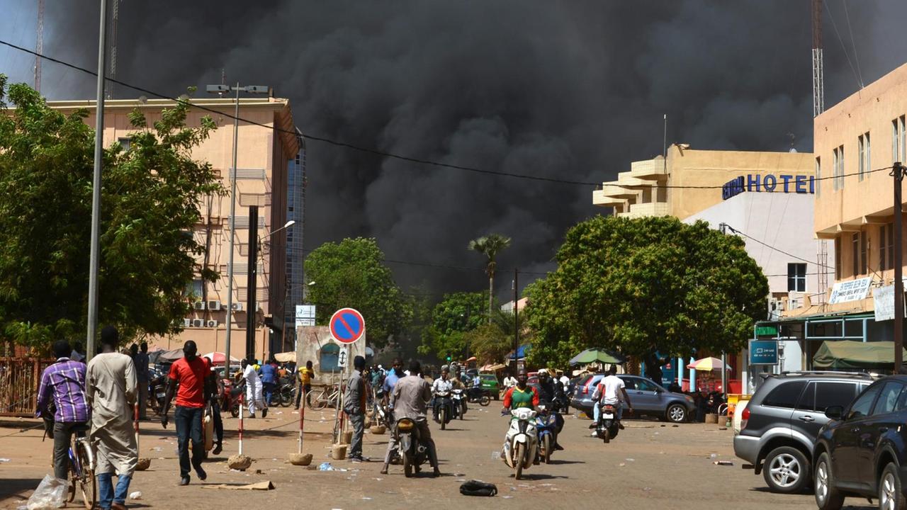 Anschlag in Ouagadougou: Menschen stehen in einiger Entfernung zu dem Anschlagsort in der Hauptstadt von Burkina Faso. Man sieht dichte, schwarze Rauchwolken. Anschlag in Ouagadougou: Menschen stehen in einiger Entfernung zu dem Anschlagsort in der Hauptstadt von Burkina Faso. Man sieht dichte, schwarze Rauchwolken.