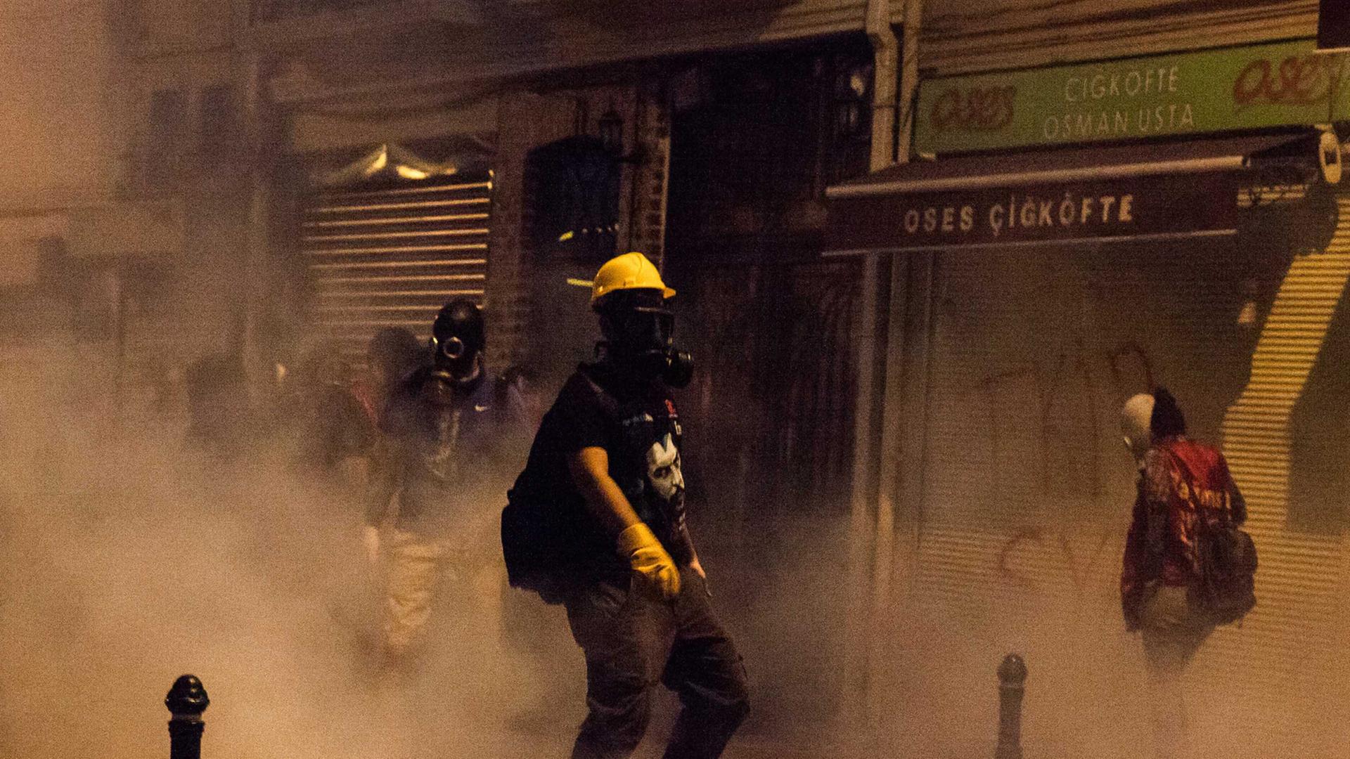 Straßenszene aus Istanbul: Ein Demonstrant mit gelbem Schutzhelm und Atemschutzmaske steht inmitten einer Rauchwolke in einer kleinen Gasse Straßenszene aus Istanbul: Ein Demonstrant mit gelbem Schutzhelm und Atemschutzmaske steht inmitten einer Rauchwolke in einer kleinen Gasse