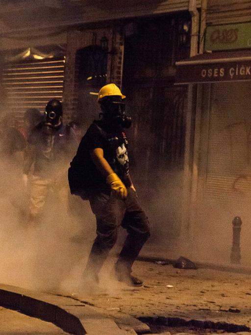 Straßenszene aus Istanbul: Ein Demonstrant mit gelbem Schutzhelm und Atemschutzmaske steht inmitten einer Rauchwolke in einer kleinen Gasse
