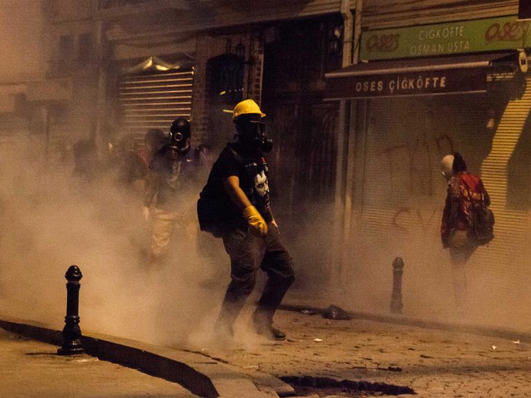 Straßenszene aus Istanbul: Ein Demonstrant mit gelbem Schutzhelm und Atemschutzmaske steht inmitten einer Rauchwolke in einer kleinen Gasse