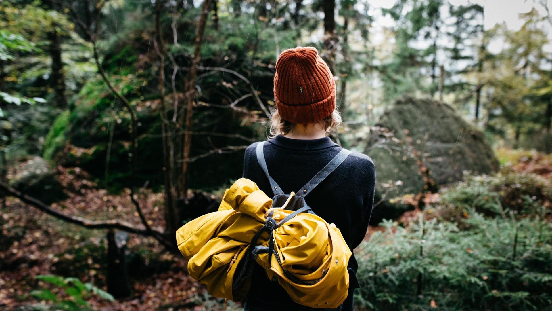 Eine Frau mit Rucksack spaziert durch einen Wald.