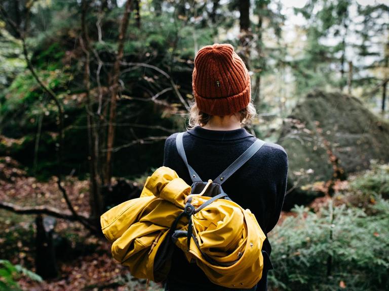 Eine Frau mit Rucksack spaziert durch einen Wald.