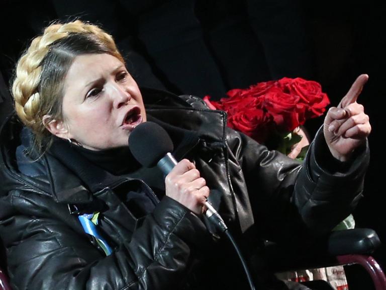 Julia Timoschenko hält im Rollstuhl sitzend eine Rede, in ihrer rechten Hand hält sie ein Mikrofon. Julia Timoschenko hält im Rollstuhl sitzend eine Rede, in ihrer rechten Hand hält sie ein Mikrofon.