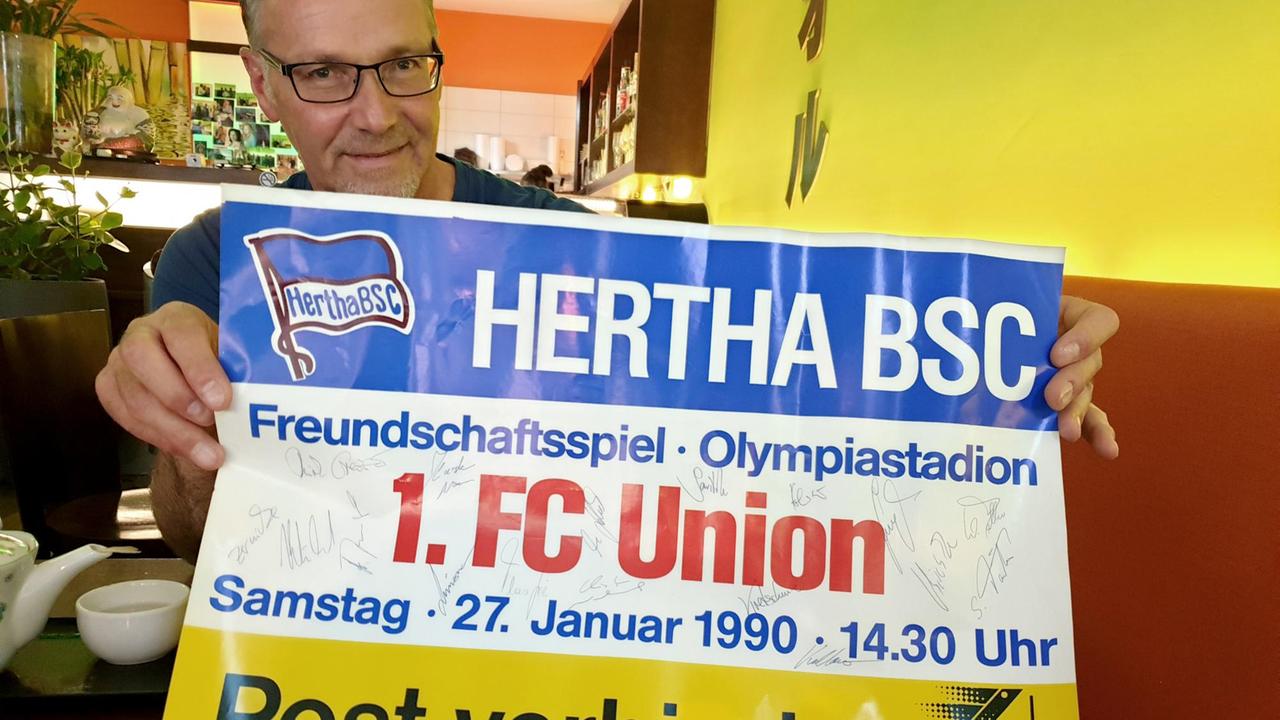 Theo Gries hält ein Plakat mit der Aufschrift „Hertha BSC Freundschaftsspiel 1. FC Union Berlin“ in der Hand und schaut in die Kamera