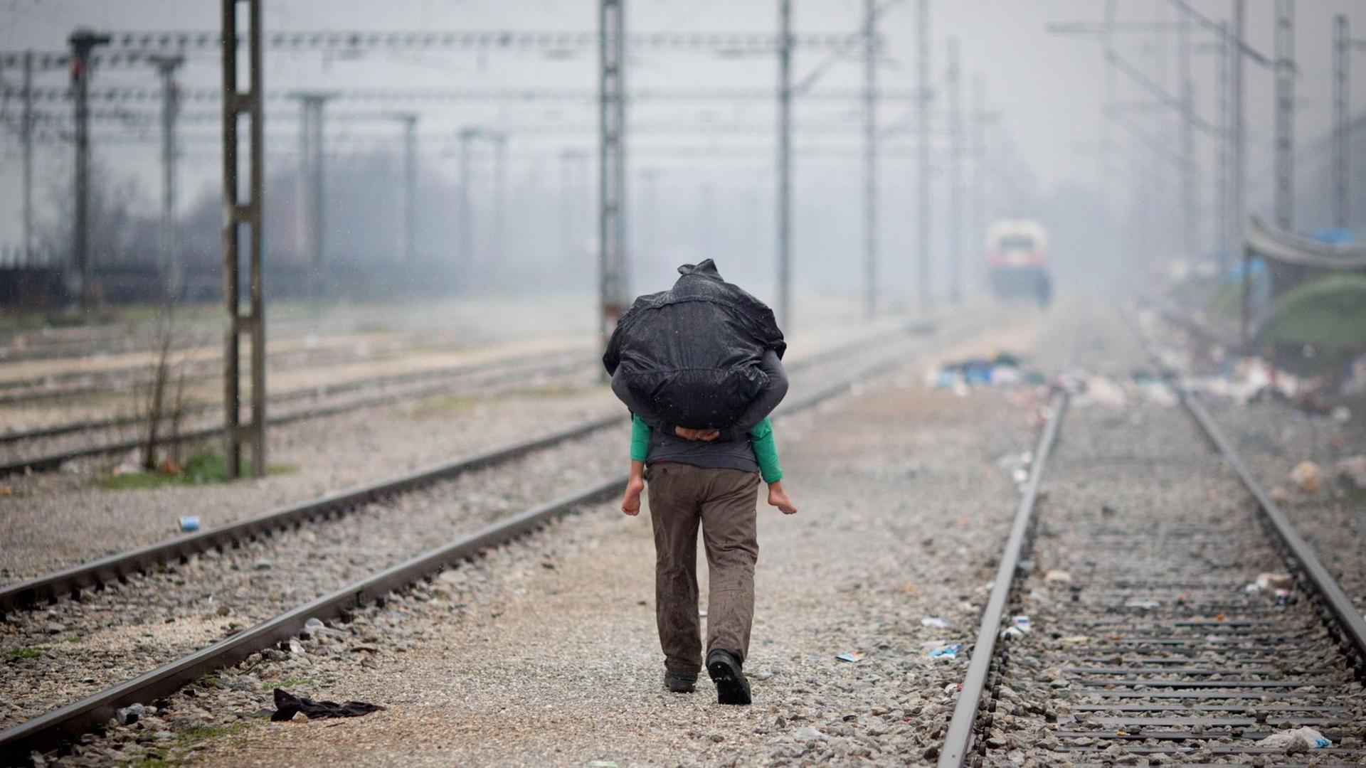 Ein Flüchtling trägt in Idomeni im Flüchtlingslager an der Grenze zwischen Griechenland und Mazedonien im strömenden Regen ein Kind auf dem Rücken. Ein Flüchtling trägt in Idomeni im Flüchtlingslager an der Grenze zwischen Griechenland und Mazedonien im strömenden Regen ein Kind auf dem Rücken.
