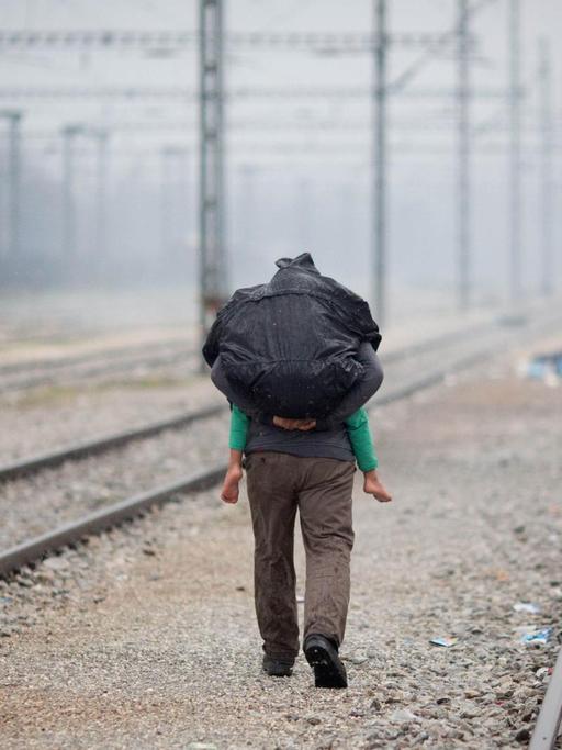 Ein Flüchtling trägt in Idomeni im Flüchtlingslager an der Grenze zwischen Griechenland und Mazedonien im strömenden Regen ein Kind auf dem Rücken.