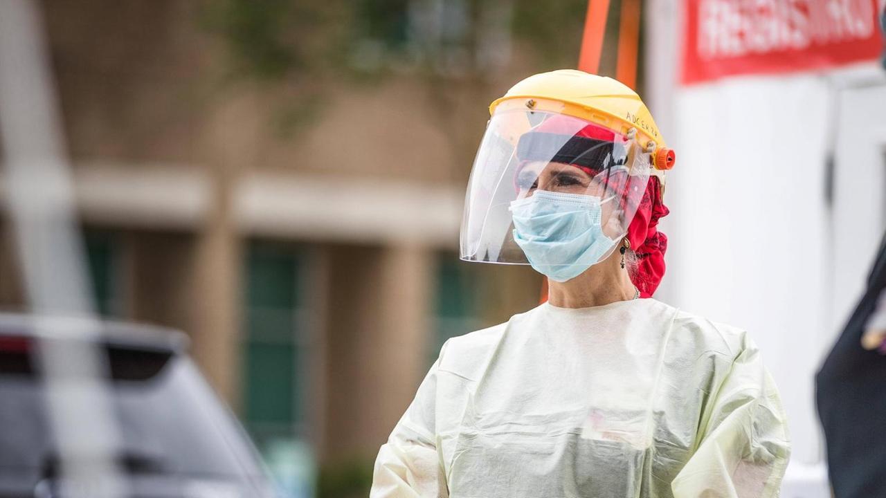 Eine Frau mit Schutzkleidung, Plexiglasmaske und gelbem Helm steht auf der Straße. Eine Frau mit Schutzkleidung, Plexiglasmaske und gelbem Helm steht auf der Straße.