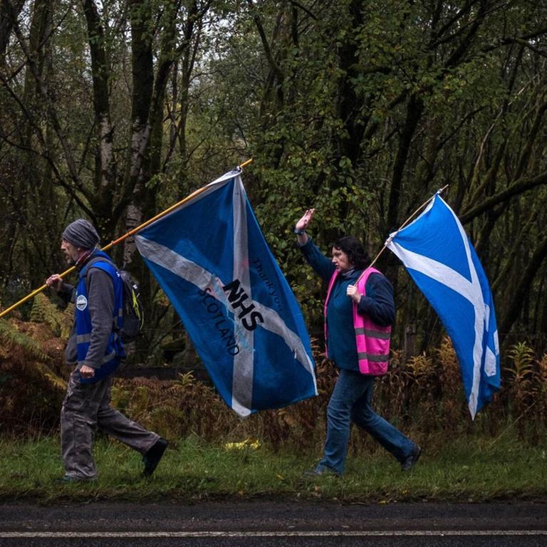 Ein Mann und eine Frau laufen mit Schottland-Flaggen an einem Waldstück entlang, 18. September 2020 