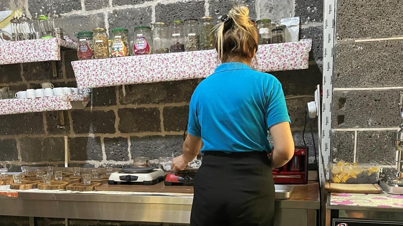 Eine junge Frau mit blondem Pferdeschwanz und T-Shirt steht in einer Küche an der Spüle und arbeitet. Eine junge Frau mit blondem Pferdeschwanz und T-Shirt steht in einer Küche an der Spüle und arbeitet.
