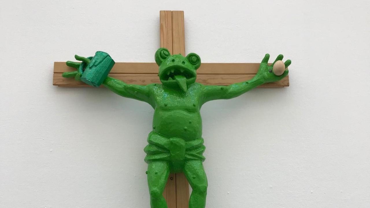 Das circa einen Meter hohe Werk von Martin Kippenberger trägt den Titel "Fred the frog rings the bell". Es zeigt einen grünen, ans Kreuz geschlagenen Frosch, der die Zunge herausstreckt und in einer Hand einen Bierkrug hält. Fotografiert ist es in der Ausstellung "Bild Macht Religion" im Kunstmuseum Bochum.