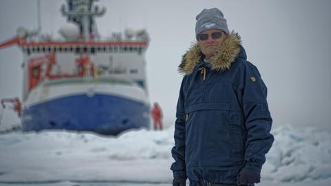 Markus Rex in Schutzkleidung mit der "Polarstern" im Hintergrund