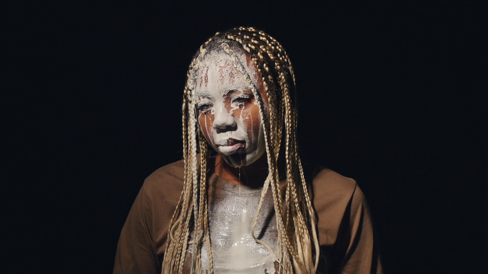 Videostill aus Martine Syms Video "Lesson LXXV" (2017). Das Bild zeigt die afroamerikanische Künstlerin Martine Syms, der weiße Flüssigkeit über das Gesicht läuft.