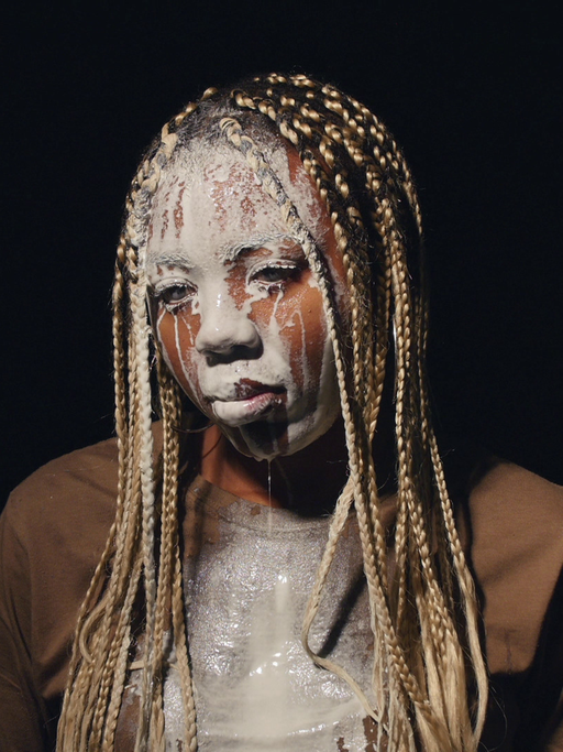 Videostill aus Martine Syms Video "Lesson LXXV" (2017). Das Bild zeigt die afroamerikanische Künstlerin Martine Syms, der weiße Flüssigkeit über das Gesicht läuft.