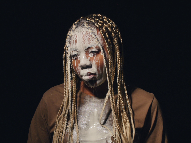 Videostill aus Martine Syms Video "Lesson LXXV" (2017). Das Bild zeigt die afroamerikanische Künstlerin Martine Syms, der weiße Flüssigkeit über das Gesicht läuft.