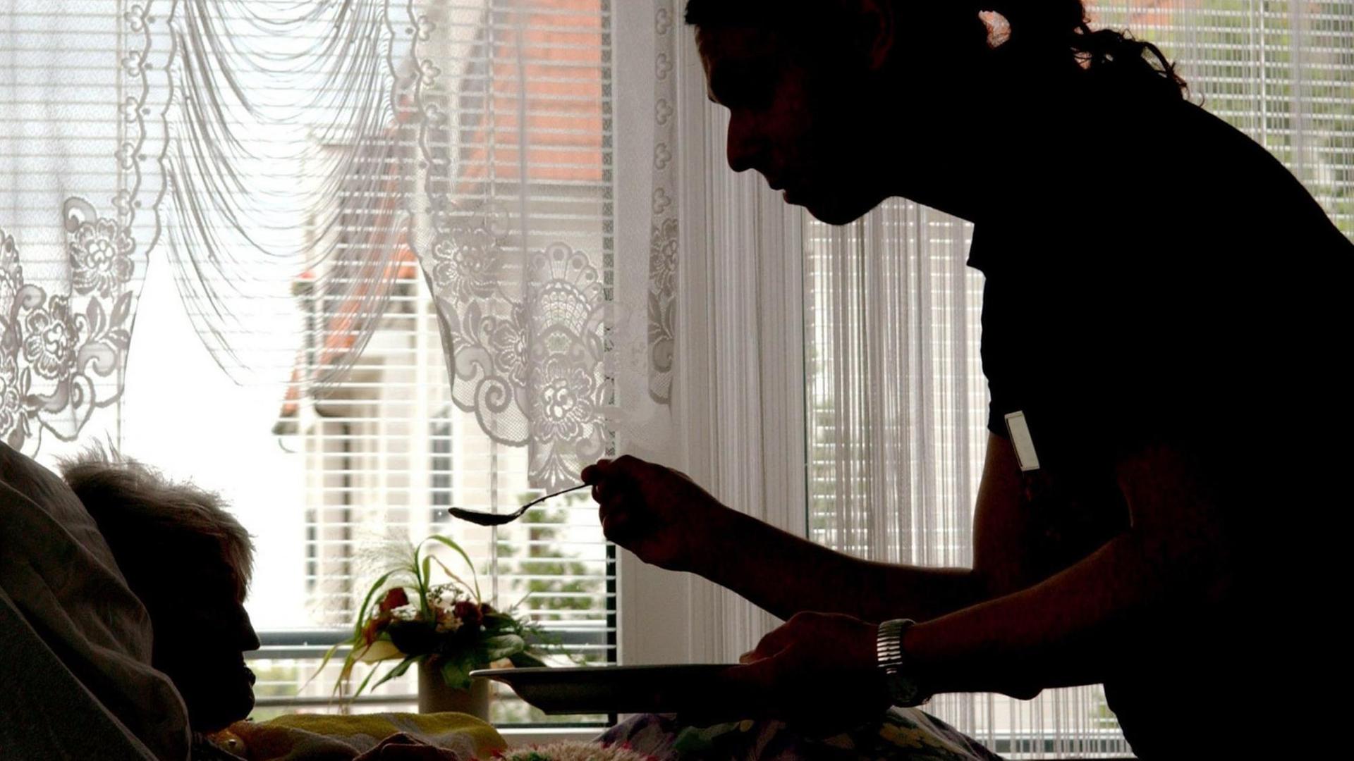Eine Pflegekraft füttert eine ältere Dame, die im Bett liegt. Eine Pflegekraft füttert eine ältere Dame, die im Bett liegt.
