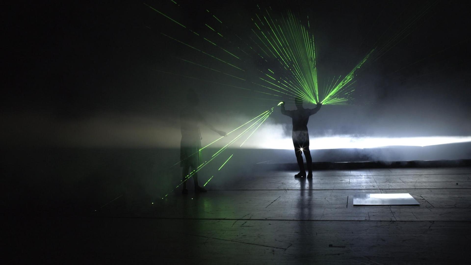 Auf dem Bild ist eine Person ganz in Schwarz zu sehen, aus dessen Händen grüne Laserstrahlen kommen. Auf dem Bild ist eine Person ganz in Schwarz zu sehen, aus dessen Händen grüne Laserstrahlen kommen.
