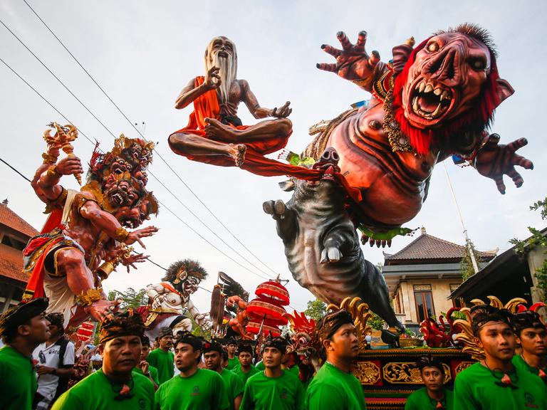 Rote monsterähnliche Figuren werden auf einer Parade von Männern in grünen T-Shirts getragen