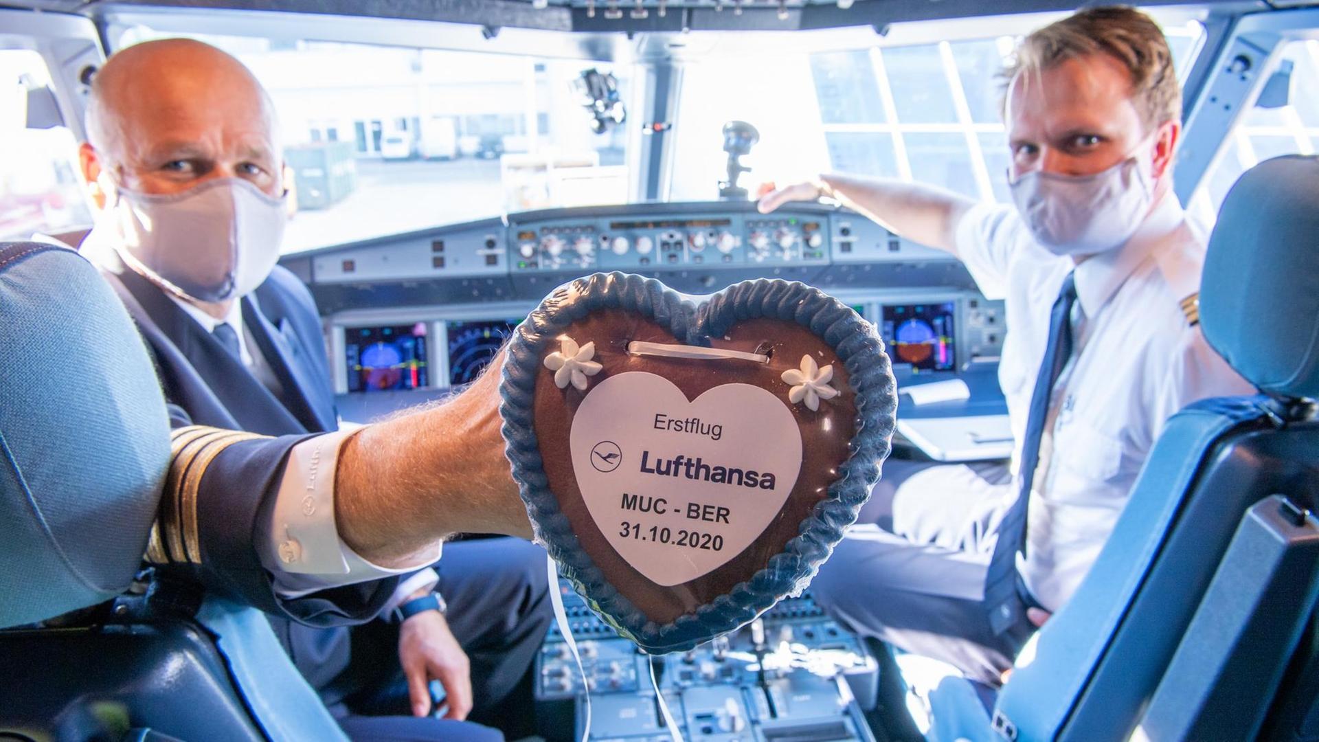Eröffnung des BER-Airports: Lufthansa Pilot Peter Etzrot und sein Co-Pilot Kai Schleicher halten im Cockpit eines Airbus vom Typ A320neo ein Lebkuchenherz mit der Aufschrift "Erstflug Lufthansa MUC-BER 31.10.2020" in der Hand.