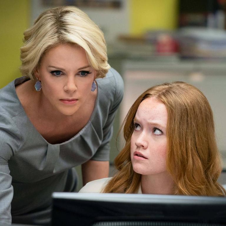 In ihrer Rolle als Megyn Kelly im Film "Bombshell" beugt sich die Schauspielerin Charlize Theron über einen Schreibtisch und schaut auf den Bildschirm einer Kollegin.