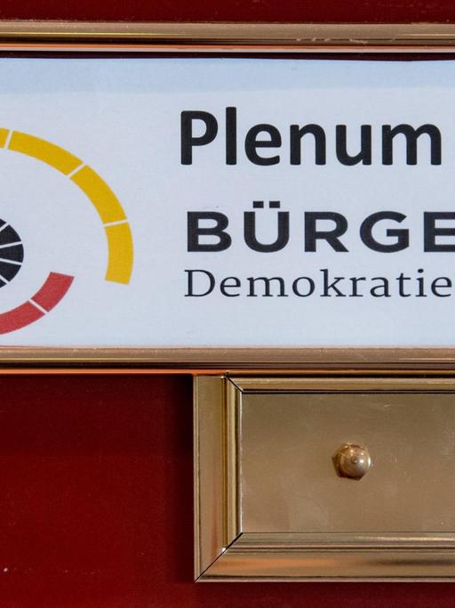 Ein Schild mit der Aufschrift Plenum - Bürgerrat Demokratie hängt am Eingang zu einem Tagungsraum in Leipzig.