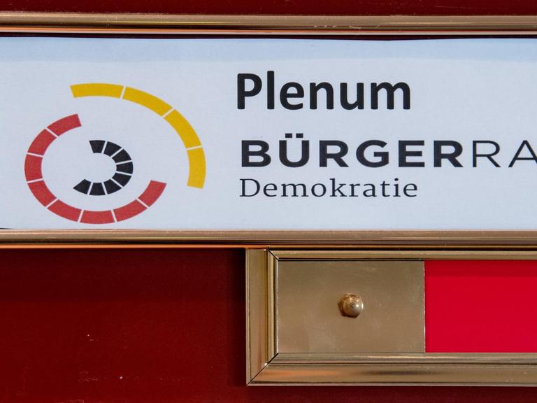 Ein Schild mit der Aufschrift Plenum - Bürgerrat Demokratie hängt am Eingang zu einem Tagungsraum in Leipzig.