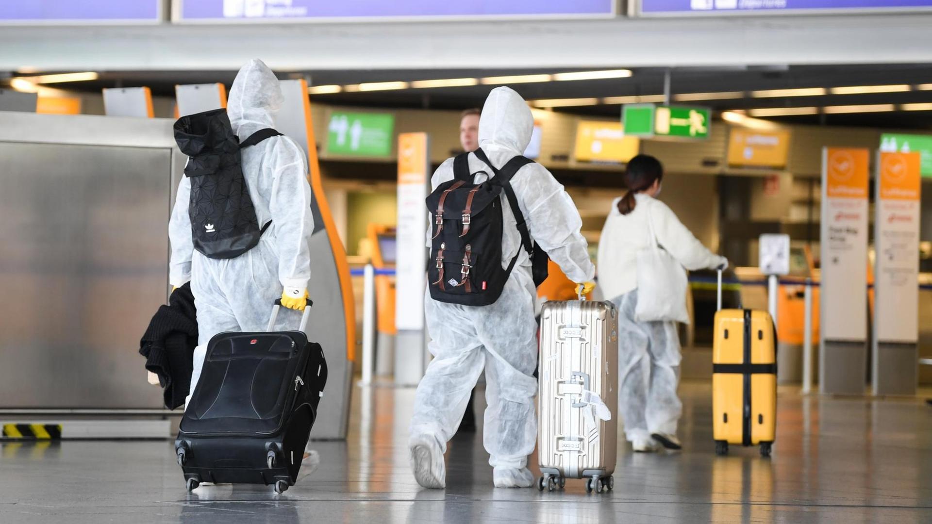 Chinesische Touristen sind in Schutzanzügen, mit Atemmasken und Handschuhen im Terminal 1 des Frankfurter Flughafens mit ihren Koffern auf dem Weg zum Flugschalter.