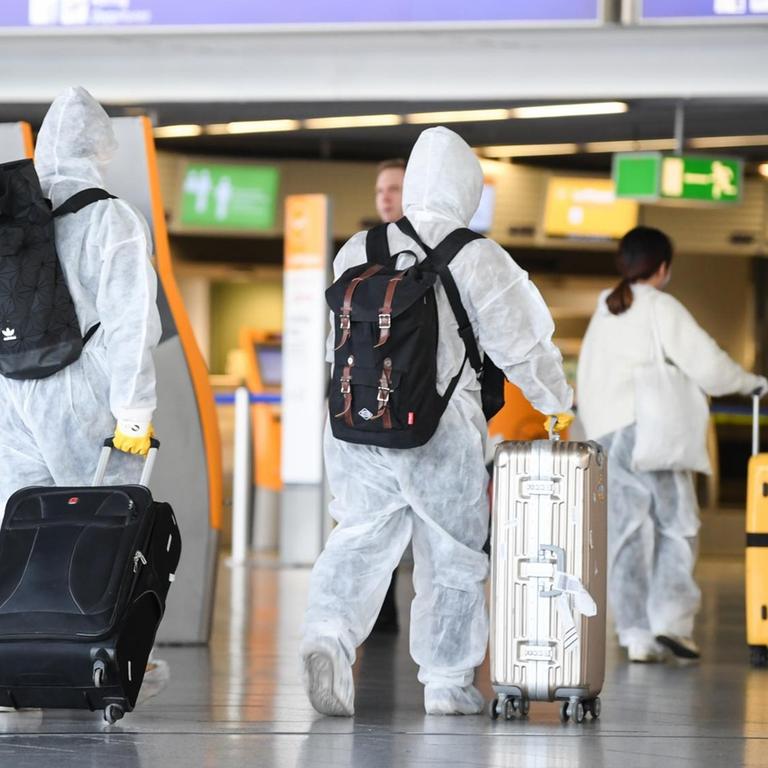 Chinesische Touristen sind in Schutzanzügen, mit Atemmasken und Handschuhen im Terminal 1 des Frankfurter Flughafens mit ihren Koffern auf dem Weg zum Flugschalter.