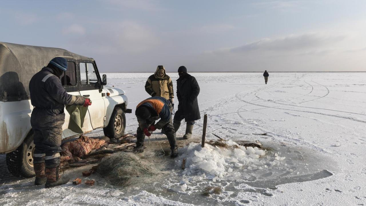 Fischer auf dem zugefrohrenen Aralsee in Kasachstan. Einer holt das Netz aus dem Eisloch.