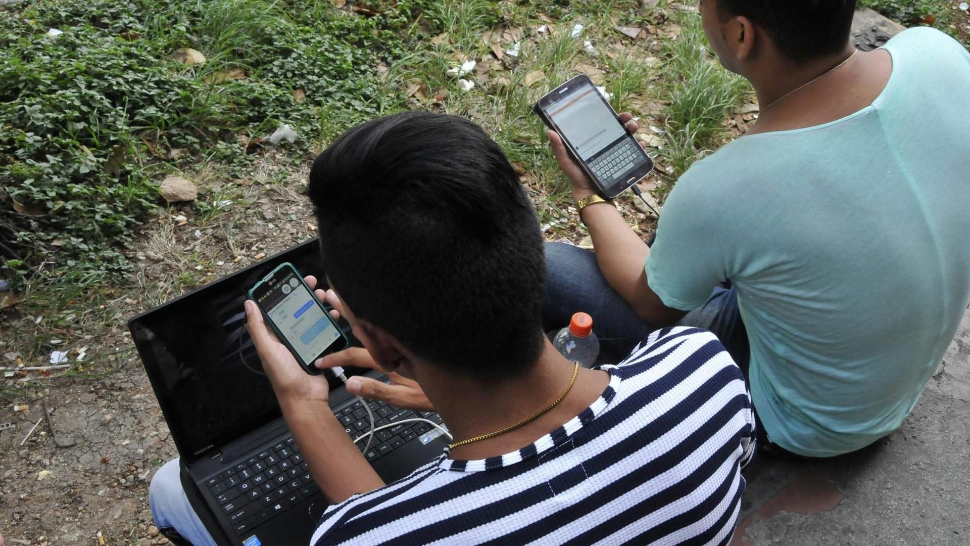 In einem Park in Havanna sitzen zwei junge Männer, die mit ihren Handys und einem Laptop im Internet sind. In einem Park in Havanna sitzen zwei junge Männer, die mit ihren Handys und einem Laptop im Internet sind.