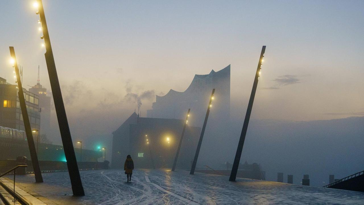 Eine Person läuft alleine in Richtung Elbphilharmonie in Hamburg während des Lockdowns. Die Stimmung ist neblig und trüb. Eine Person läuft alleine in Richtung Elbphilharmonie in Hamburg während des Lockdowns. Die Stimmung ist neblig und trüb.