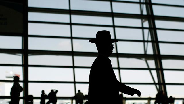Abflugshalle des Flughafens Ben Gurion in Israel: durch die einfallende Sonne liegen die Streben der Glasfront und die vorübergehenden Menschen im Schatten, markant im Vordergrund ist die Silhouette eines orthodoxen Juden zu sehen