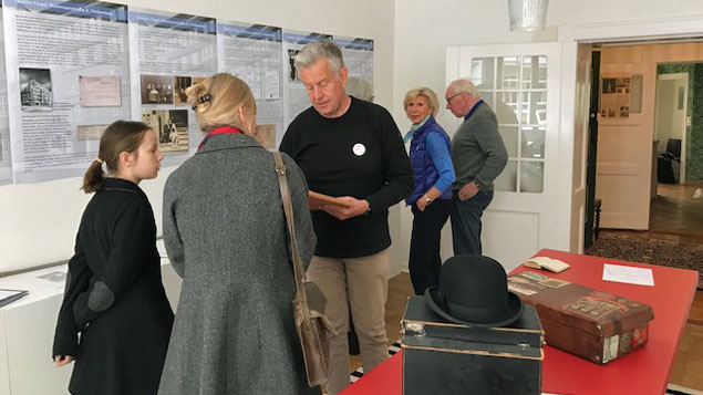 Im Ausstellungsraum im Gartenhaus schauen sich Besucher Wandtafeln an. In der Mitte des Raums sind Alltagsgegenstände der früheren Bewohner ausgestellt: Koffer, Hut, Buch. Im Ausstellungsraum im Gartenhaus schauen sich Besucher Wandtafeln an. In der Mitte des Raums sind Alltagsgegenstände der früheren Bewohner ausgestellt: Koffer, Hut, Buch.