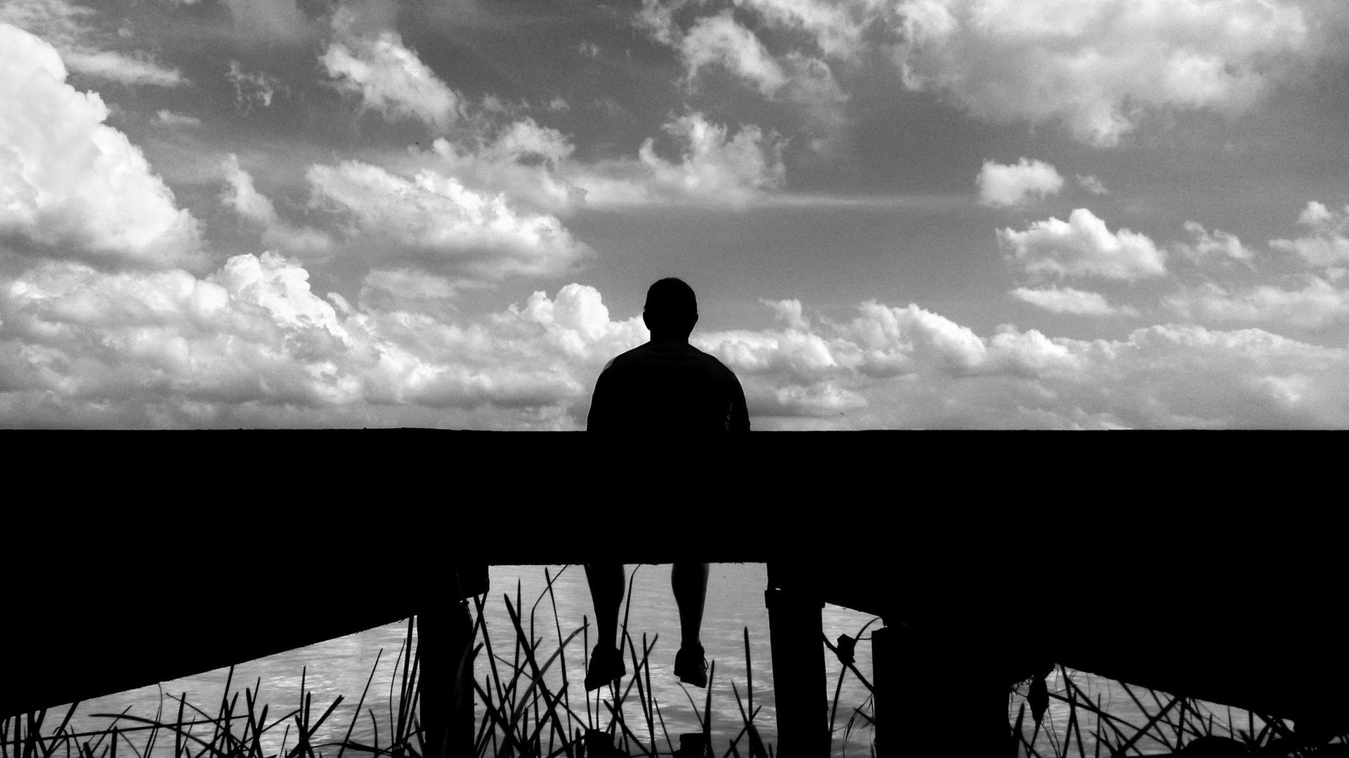 Ein Mann sitzt am 04.08.2013 auf einem Steg am Selenter See (Schleswig-Holstein).
