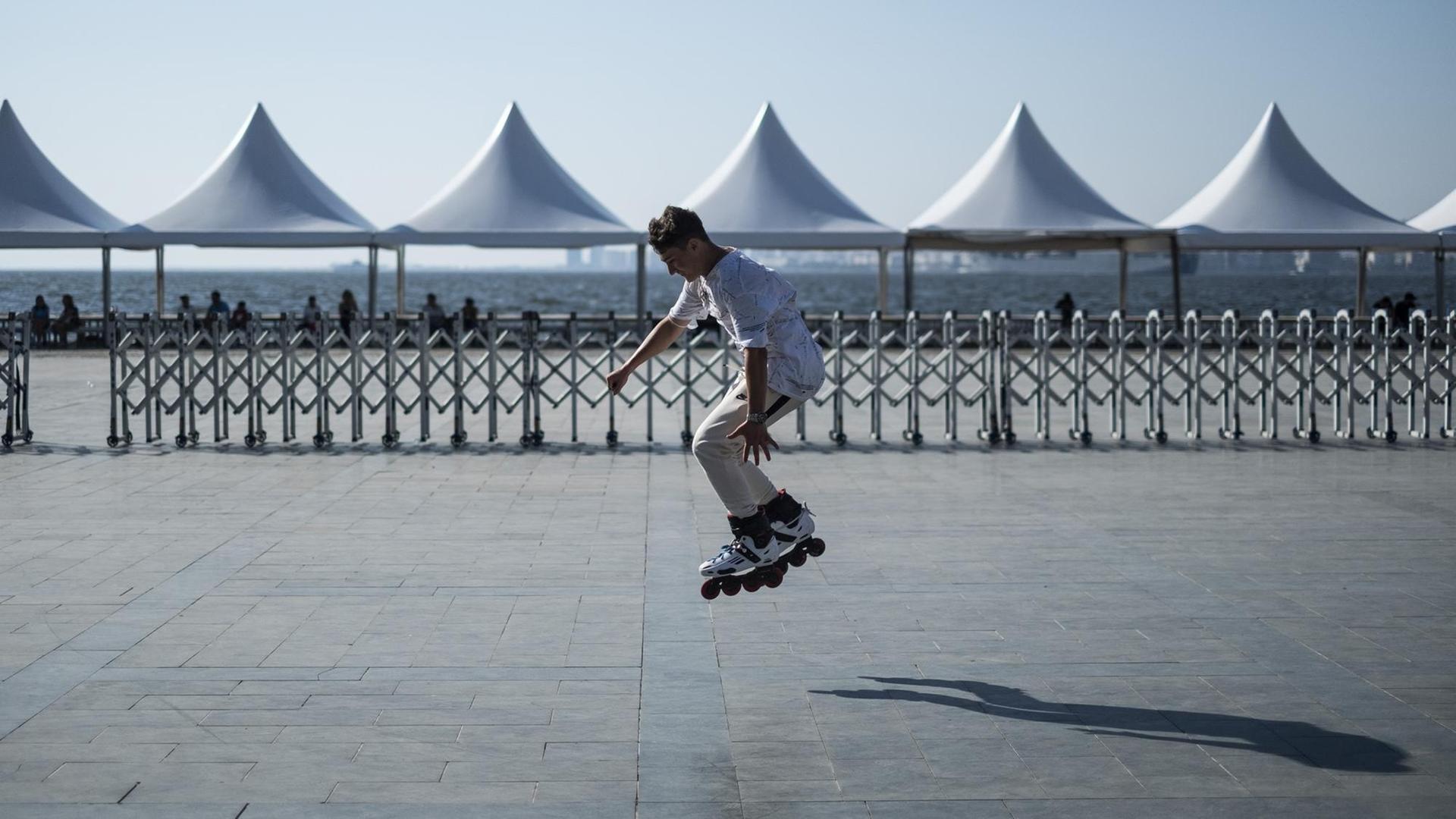 Ein junger Mann fährt Rollerblades. Im Hintergrund stehen Pavillons an einer Strandpromenade. Ein junger Mann fährt Rollerblades. Im Hintergrund stehen Pavillons an einer Strandpromenade.