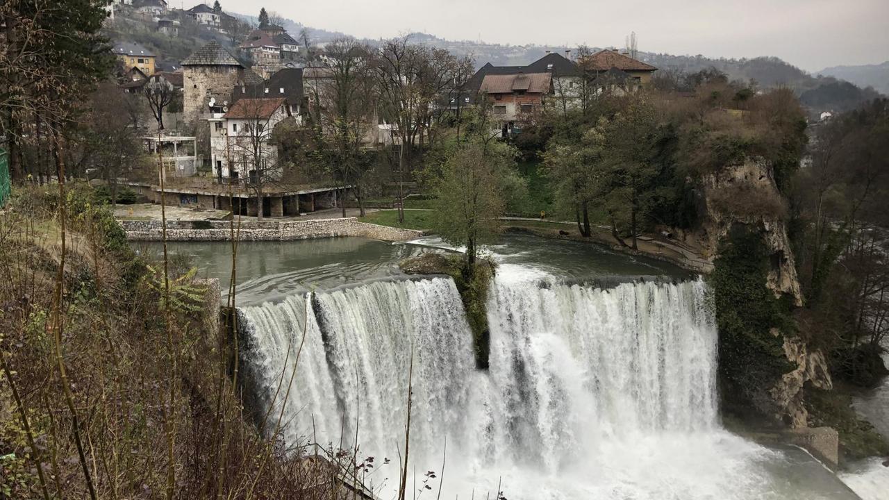Wasserfall umringt von Häusern und Natur Wasserfall umringt von Häusern und Natur
