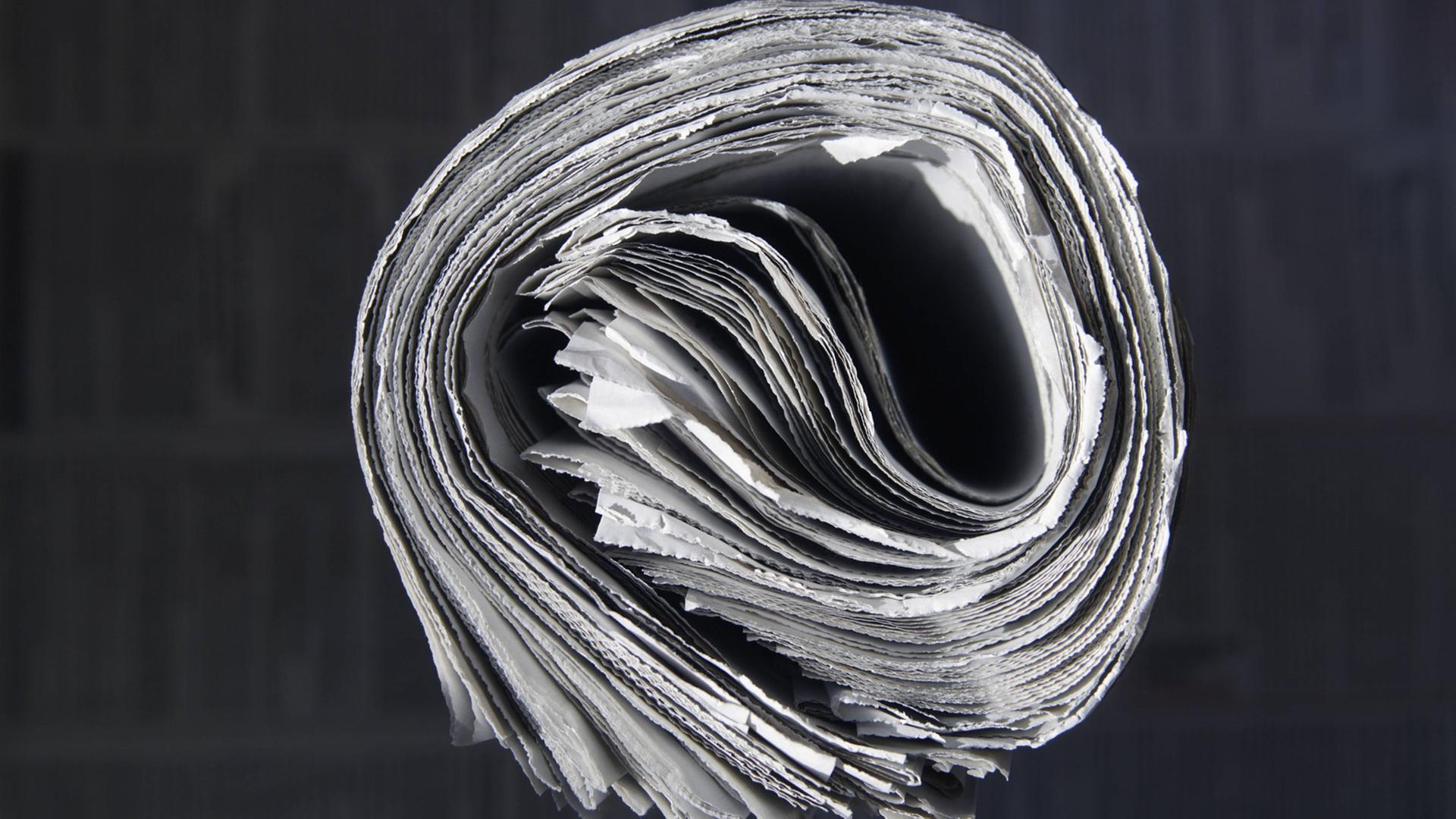 Eine eingerollte Zeitung im Querschnitt vor einem schwarzen Hintergrund. Eine eingerollte Zeitung im Querschnitt vor einem schwarzen Hintergrund.