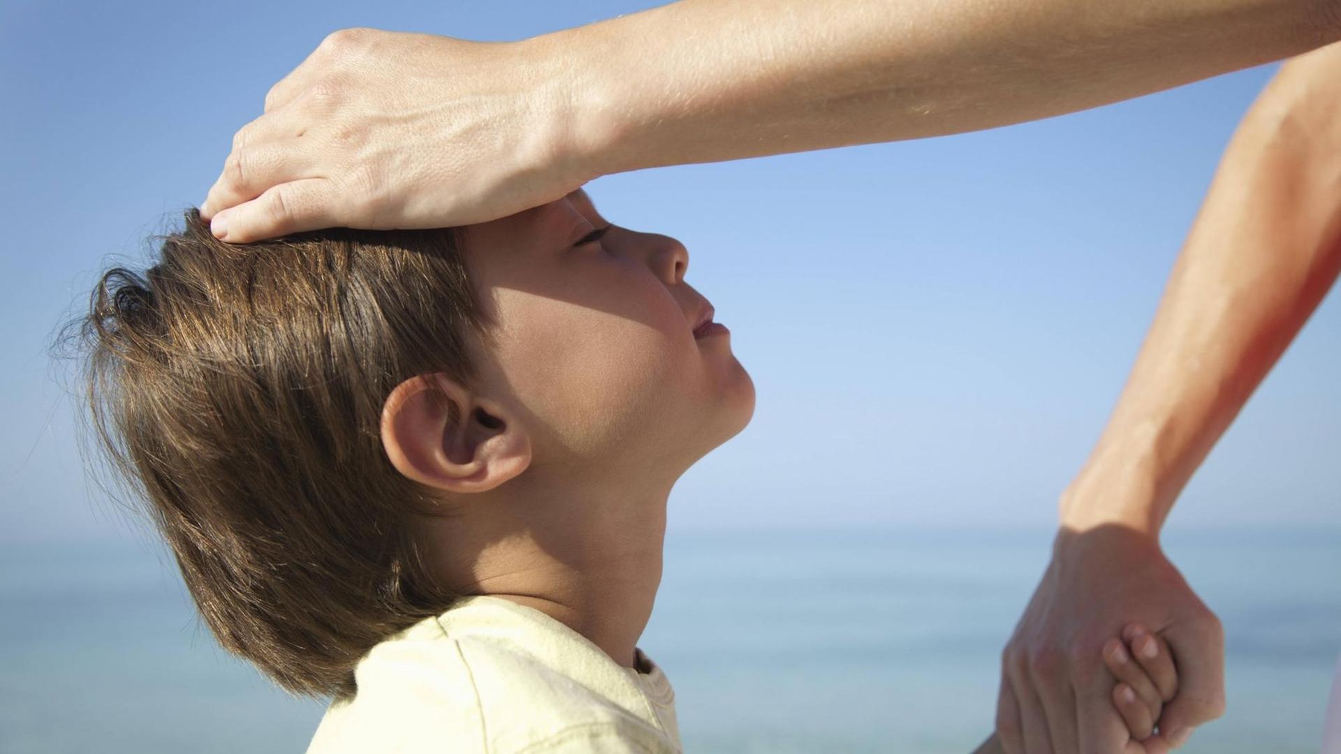 Kind in der Sonne, die Hand seiner Mutter liegt auf seinem Kopf. Kind in der Sonne, die Hand seiner Mutter liegt auf seinem Kopf.