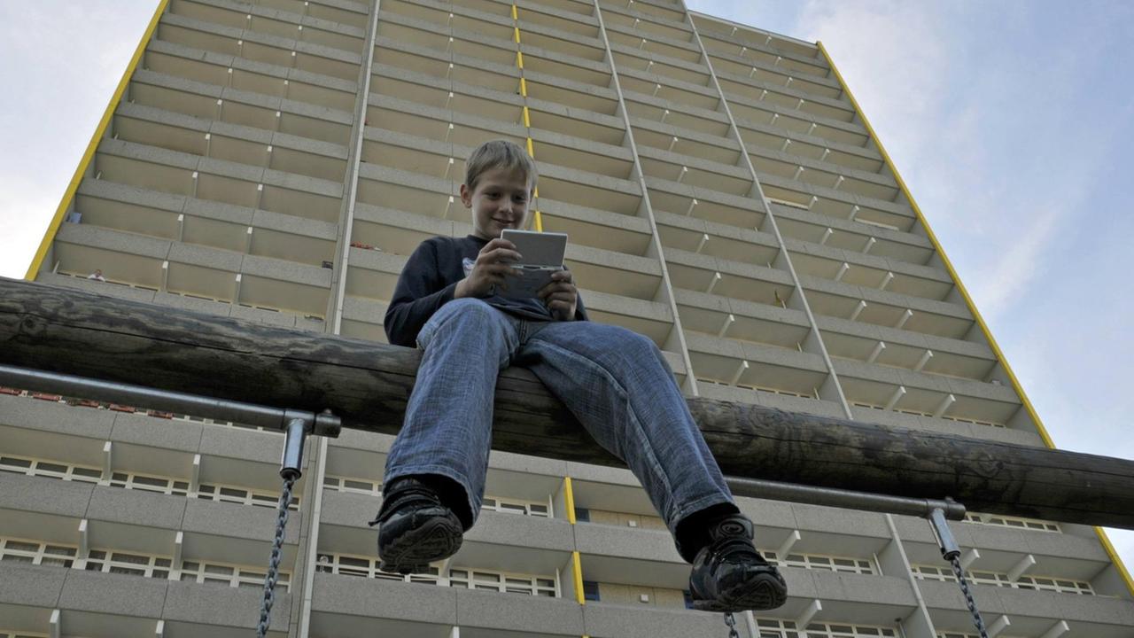 EIn neunjaehriger Junge spielt mit seinem Nintendo vor einem Hochhaus in Chorweiler, am Himmel fliegt ein Flugzeug. EIn neunjaehriger Junge spielt mit seinem Nintendo vor einem Hochhaus in Chorweiler, am Himmel fliegt ein Flugzeug.