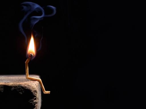 Ein brennendes Streichholz symbolisiert einen Menschen, der niedergeschlagen auf einer Kante sitzt.