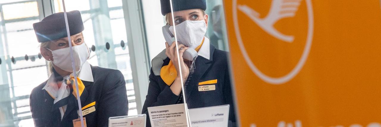 03.06.2020, Bayern, München: Zwei Lufthansa-Mitarbeiterinnen mit Mund-Nasen-Sschutzmaske und hinter Plexiglasscheiben fertigen am Flughafen-Terminal 2 die Gäste für den Flug in die USA ab. Lufthansa nimmt am 03.06.2020 die Verbindung München-Los Angeles vom Flughafen München wieder auf. Foto: Peter Kneffel/dpa | Verwendung weltweit 03.06.2020, Bayern, München: Zwei Lufthansa-Mitarbeiterinnen mit Mund-Nasen-Sschutzmaske und hinter Plexiglasscheiben fertigen am Flughafen-Terminal 2 die Gäste für den Flug in die USA ab. Lufthansa nimmt am 03.06.2020 die Verbindung München-Los Angeles vom Flughafen München wieder auf. Foto: Peter Kneffel/dpa | Verwendung weltweit