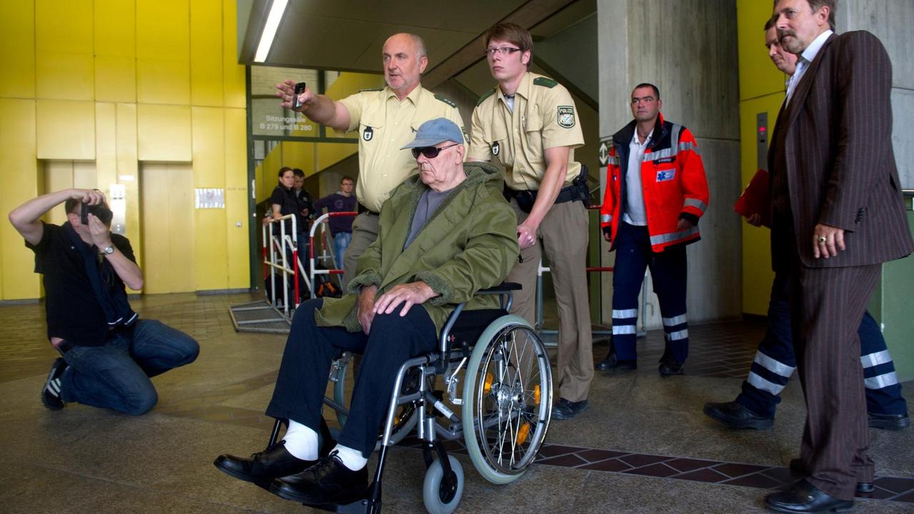 Der wegen Beihilfe zum Mord angeklagte ehemalige Wächter des deutschen Vernichtungslagers Sobibor, der US-Bürger John "Iwan" Demjanjuk, wird in einem Rollstuhl sitzend von Polizisten durch das Landgericht in München gefahren. Der wegen Beihilfe zum Mord angeklagte ehemalige Wächter des deutschen Vernichtungslagers Sobibor, der US-Bürger John "Iwan" Demjanjuk, wird in einem Rollstuhl sitzend von Polizisten durch das Landgericht in München gefahren.