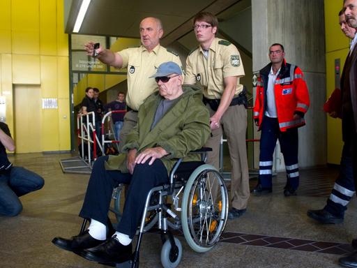 Der wegen Beihilfe zum Mord angeklagte ehemalige Wächter des deutschen Vernichtungslagers Sobibor, der US-Bürger John "Iwan" Demjanjuk, wird in einem Rollstuhl sitzend von Polizisten durch das Landgericht in München gefahren.